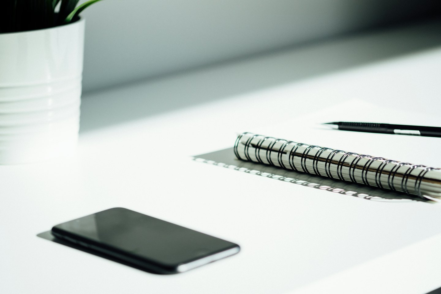 Smartphone, notebook, and pen on a white desk.